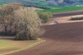 Scenic View Of Farming BlueTractor With Red Harrow Which Plowing And Spraying Brown Spring Field. Small Blue Tractor Working On Br