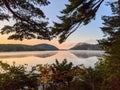 Scenic view of green forest and hills reflecting on a tranquil lake at a foggy sunset