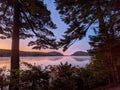 Scenic view of green forest and hills reflecting on a tranquil lake at a foggy sunset