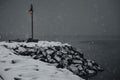 Scenic view of a lamp on a snow-covered rocky coast illuminating the bench on a foggy winter day Royalty Free Stock Photo