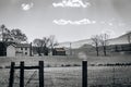 Scenic view of old wooden cabins on a grassy hill in a fenced area in grayscale Royalty Free Stock Photo