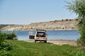 Scenic view over wide river with old car, parked on it`s bank. Beautiful natural countryside landscape with blue sunny sky. Summe Royalty Free Stock Photo