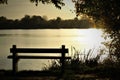 Scenic view of the reflection of bright sun in the lake with wooden bench on the shore