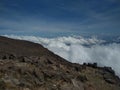 Scenic view of a rocky mountain slope above the clouds under the blue sky