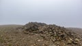 A scenic view of a rocky mountain summit with a stony cairn under a misty sky