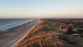 Scenic view of a secluded beach, surrounded by rolling hills, lush vegetation, and houses at sunset