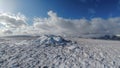 A scenic view of snowy mountain summit trig point cairn under a majestic blue sky and white clouds