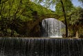 Scenic view of a waterfall flowing under an old stone bridge surrounded by greenery Royalty Free Stock Photo