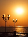 Scenic view of waterfront with lanterns backlit by setting sun and with ships in the roadstead Royalty Free Stock Photo