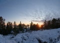 Scenic View on Winter Sunset Over Sea behind forest on coastline, Snowy foreground with very big stones covered by fresh snow, Royalty Free Stock Photo