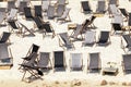 Scenic water view of many empty black wooden deckchair loungers on sand river or sea ocean beach. Rows of deckchair on