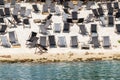 Scenic water view of many empty black wooden deckchair loungers on sand river or sea ocean beach. Rows of deckchair on