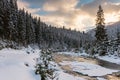 Scenic winter sunset landscape with small winding mountain river, fluffy snow, snowy fir trees and colorful sky with clouds Royalty Free Stock Photo
