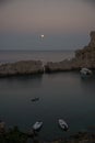 Scenicc view of coastline with calm water, boats and full moon at sunset. Rhodes, Greece Royalty Free Stock Photo