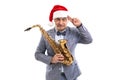 Sceptical man wears in Santa's hat holds saxophone while raising hand to head on studio background