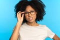 Sceptical mistrustful African American girl adjusts glasses, suspicious looking at camera. Studio.