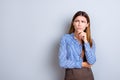 Sceptical young business lady is unsure what to do. She has focused grimace, wearing strict formal wear, standing on pure light b Royalty Free Stock Photo