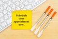Schedule your appointment now message with disposable vaccine needle with keyboard with a sticky note