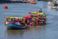 A farmer and two beautiful peasant women on a raft full of vegetables pulled by a boat.