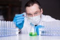 Scholar in mask and rubber gloves conducts researching in the lab. Scientist dripping by pipette green reactant into a