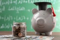 Scholarship concept. Glass jar with coins, piggy bank, graduation cap and dollar banknotes on wooden table