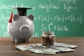 Scholarship concept. Glass jar with coins, piggy bank, graduation cap and dollar banknotes on wooden table