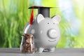 Scholarship concept. Glass jar with coins, piggy bank and graduation cap on grey table