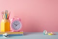 School accessories concept. Photo of stand for pencils alarm clock stack of notebooks mini stapler and adhesive tape on pink wall Royalty Free Stock Photo