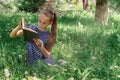 A school-age girl reading a book sitting on the grass in the park. Front view. Royalty Free Stock Photo