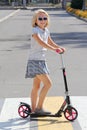 School-aged girl riding a scooter. Crosses the road on a pedestrian crossing. Royalty Free Stock Photo