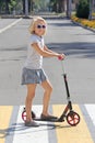 School-aged girl riding a scooter. Crosses the road on a pedestrian crossing. Royalty Free Stock Photo