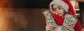 A school-aged girl in a Santa Claus hat, puzzled and surprised, holds cash in dollar bills. Christmas and business horizontal Royalty Free Stock Photo