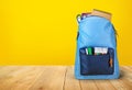 School bag backpack with notebooks on wooden table and yellow background. Royalty Free Stock Photo