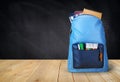 School bag with stationery and notebooks in front of blackboard