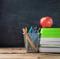 School books with stationery and apple on blackboard background Royalty Free Stock Photo