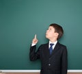 School boy in black suit show finger up gesture and wonder, point on green chalkboard background, education concept Royalty Free Stock Photo