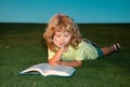 School boy with a book having a rest outdoor. Child boy is reading a book on the spring park. Relaxing on the grass in Royalty Free Stock Photo