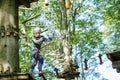 School boy in forest adventure park. Acitve child, kid in helmet climbs on high rope trail. Agility skills and climbing