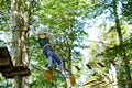 School boy in forest adventure park. Acitve child, kid in helmet climbs on high rope trail. Agility skills and climbing