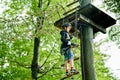 School boy in forest adventure park. Acitve child, kid in helmet climbs on high rope trail. Agility skills and climbing