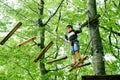 School boy in forest adventure park. Acitve child, kid in helmet climbs on high rope trail. Agility skills and climbing