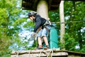 School boy in forest adventure park. Acitve child, kid in helmet climbs on high rope trail. Agility skills and climbing