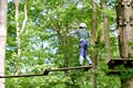 School boy in forest adventure park. Acitve child, kid in helmet climbs on high rope trail. Agility skills and climbing