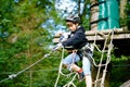 School boy in forest adventure park. Acitve child, kid in helmet climbs on high rope trail. Agility skills and climbing