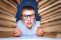 School boy in glasses sitting between two piles of books and look at camera grimaces Royalty Free Stock Photo