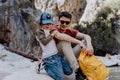 School boy and his dad with yellow backpack sits on a riverside rock in the canyon with mountain cliffs in the