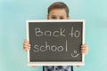 School boy holds blackboard with inscription back to school made with piece of chalk.