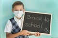 school boy in medical mask holds blackboard with inscription back to school made with piece of chalk. Royalty Free Stock Photo