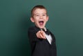 School boy point the finger near blank chalkboard background, dressed in classic black suit, group pupil, education concept