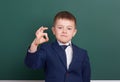 School boy show ok sign, portrait near green blank chalkboard background, dressed in classic black suit, one pupil, education conc Royalty Free Stock Photo